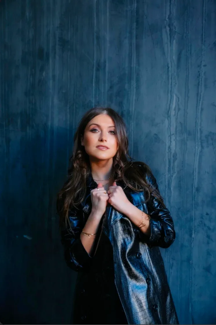Elle Winter in a black leather jacket against a blue wall.